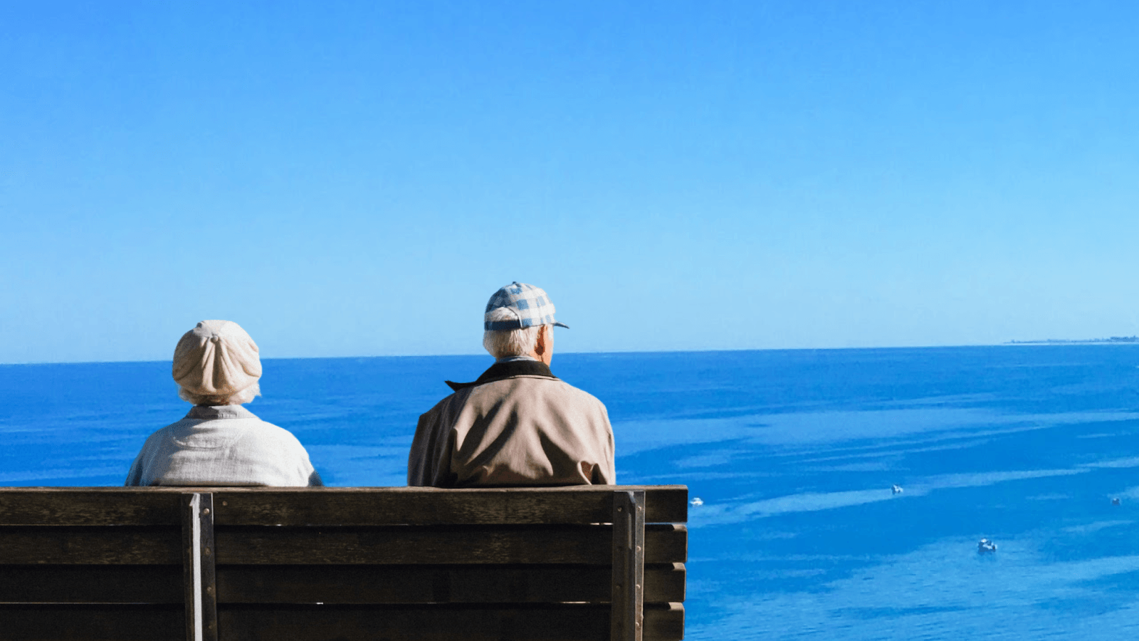 An old couple sitting on a bench in front of the ocean