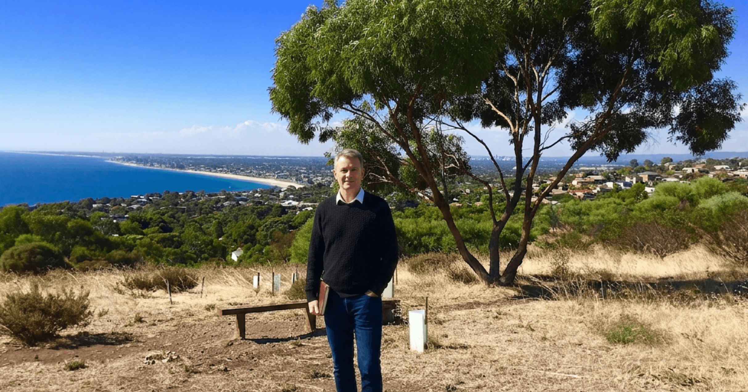 Middle-aged man standing close to the camera, behind him the view of Adelaide from the hill top