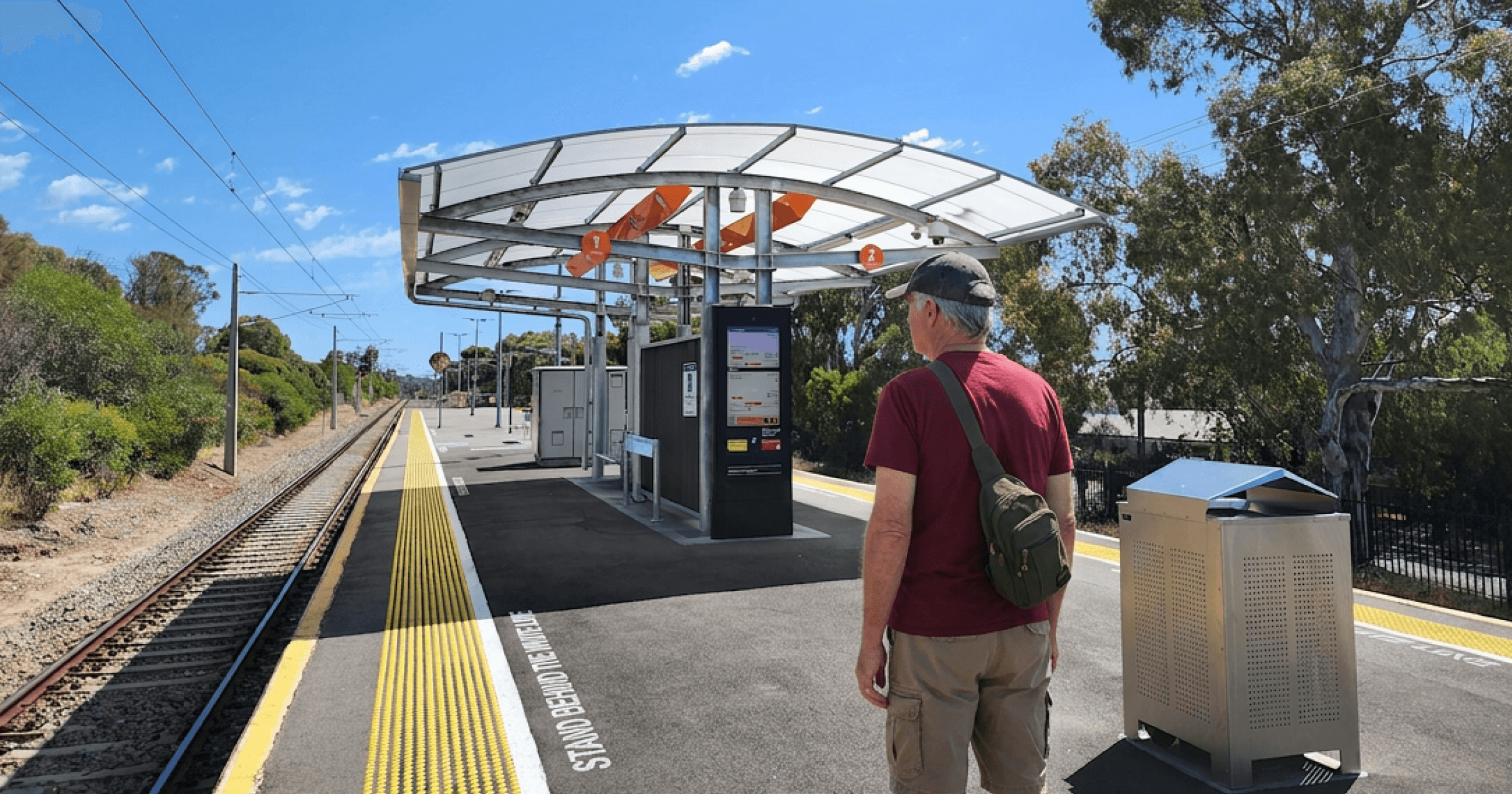 Man standing on the train platform in a t-shirt and shorts, facing away from the camera
